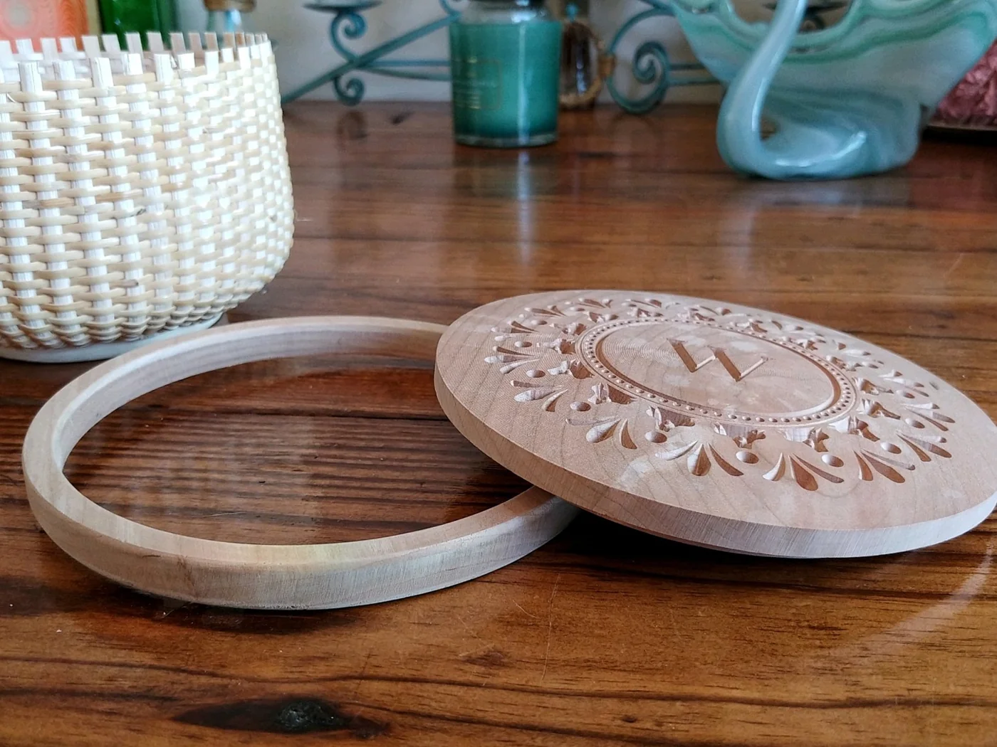 A carved wooden basket lid and fitted rim on a wooden table beside a woven basket